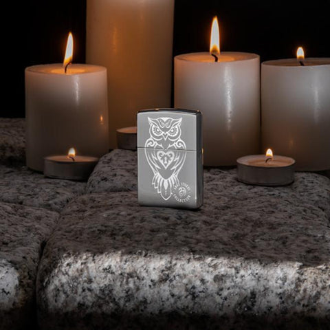 Lifestyle image of Anne Stokes High Polished Chrome Owl Lighter standing on cobblestone with lit candles in the background