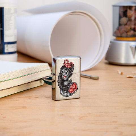 Lifestyle image of stylised Tattoo Design Brushed Chrome Windproof Lighter on a desk with art material