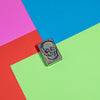 Lifestyle image of Geometric Skull Design Street Chrome Windproof Lighter laying flat on neon multicoloured background