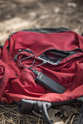 Black HeatBank 3 Rechargeable Hand Warmer laying on a backpack charging phone in the woods