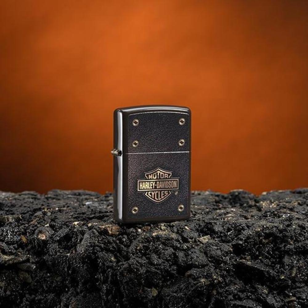 Lifestyle image of Harley-Davidson® Logo Leather Design Brown Windproof Lighter standing on asphalt with an orange background