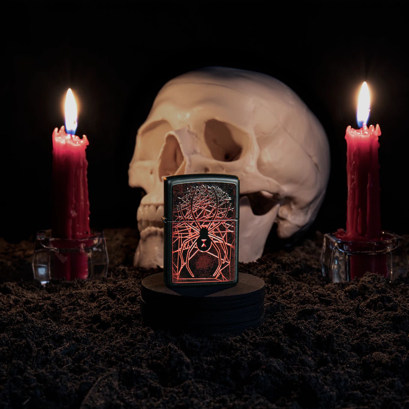 Lifestyle image of Spider Design Texture Print Black Matte Windproof Lighter standing with a skull and lit candles behind it.