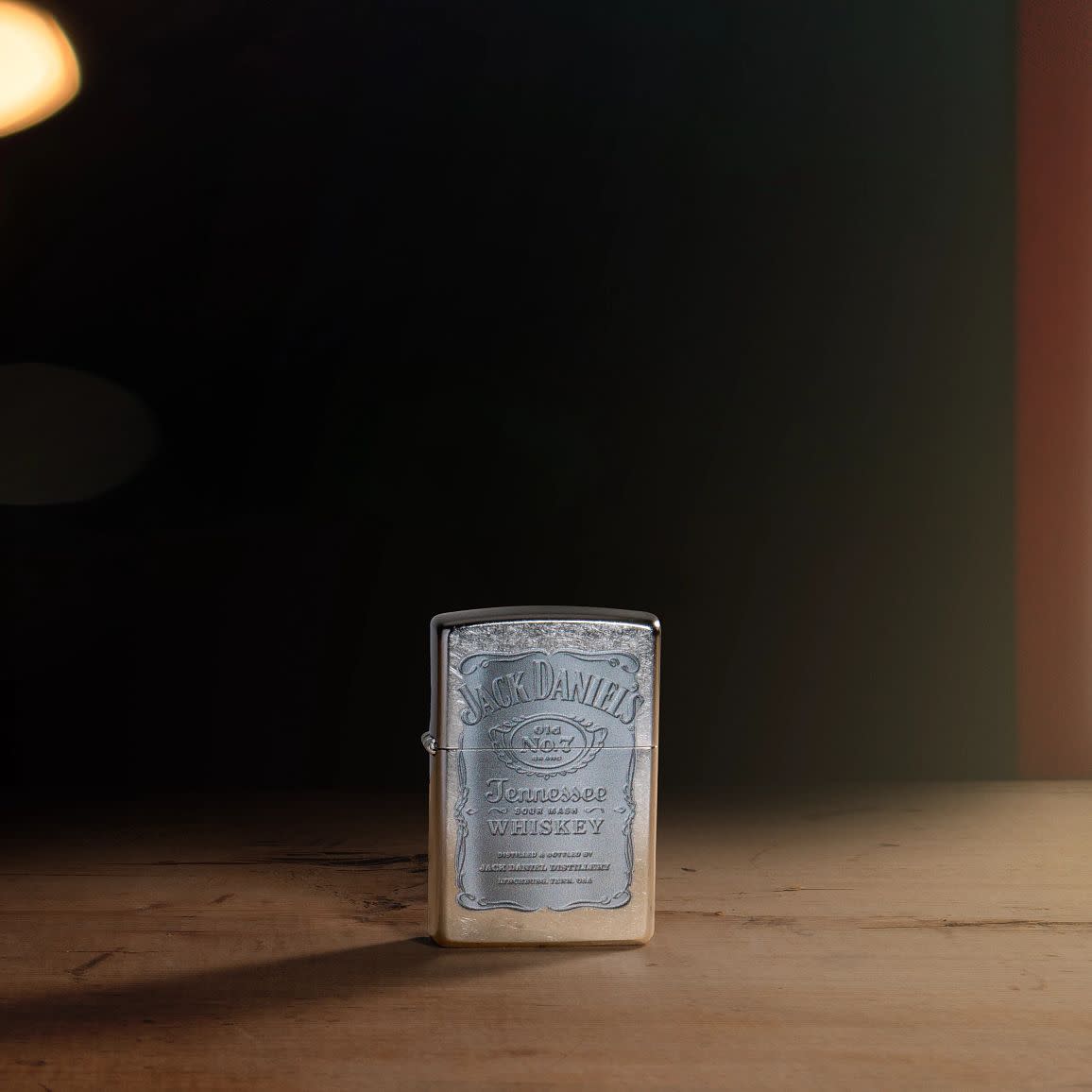 Lifestyle image of Jack Daniel's Silver Logo Street Chrome Windproof Lighter standing on a bar, with a dark background.