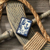 Lifestyle image of Nautical Design Navy Matte Windproof Lighter laying on a ship's helm with rope around it.