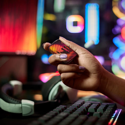 Lifestyle image of Zippo Cyber City Design 540 Color Matte Windproof Lighter held in hand in a gaming set up, with a keyboard, headset, and RGB lights behind it.