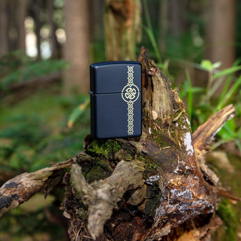 Lifestyle image of Celtic Laser Engraved Black Matte Windproof Lighter standing in the woods on a tree roots.