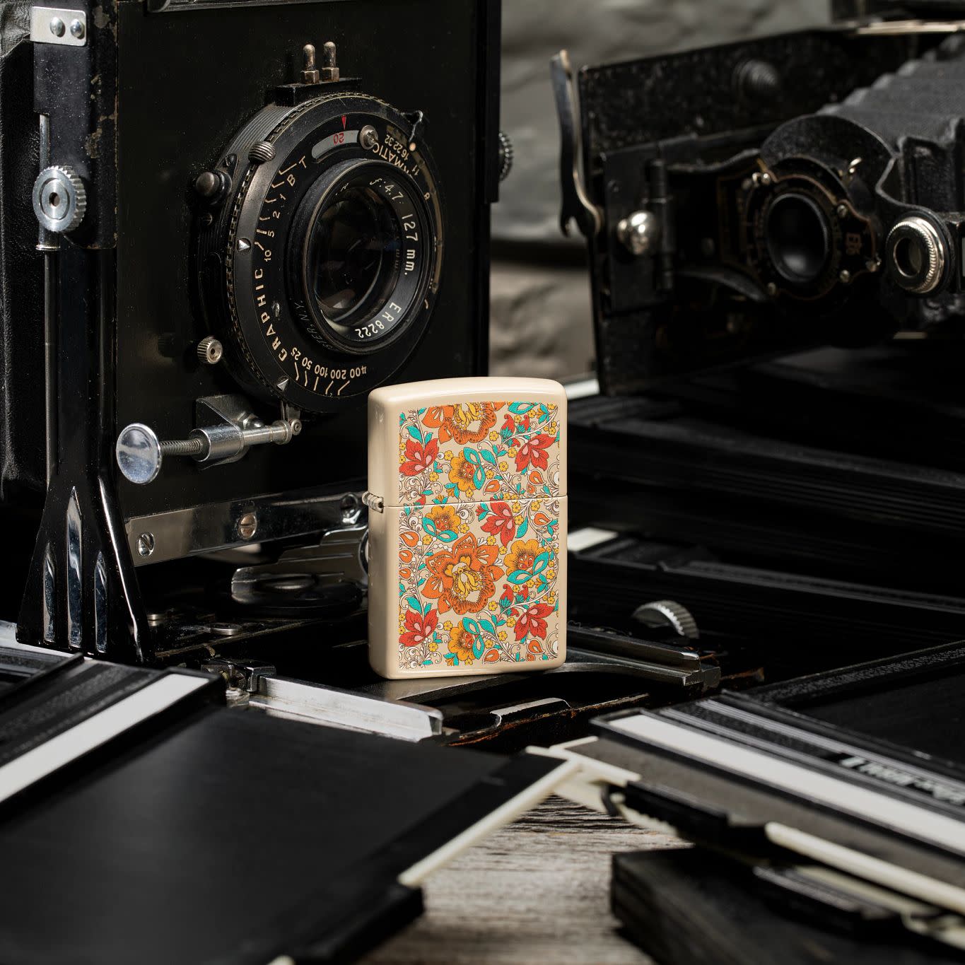 Lifestyle image of Vintage Floral Design Flat Sand Windproof Lighter standing with vintage cameras behind it.