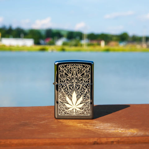 Lifestyle image of Cannabis Design Laser Two Tone Black Ice Windproof Lighter standing on a railing with a lake behind it.