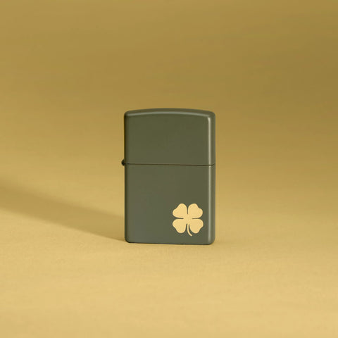 Lifestyle image of Four Leaf Clover Green Matte Windproof Lighter standing in a yellow background.