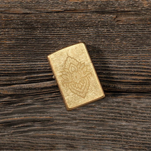 Lifestyle image of Henna Tattoo Design Tumbled Brass Windproof Lighter laying flat on a wooden table.