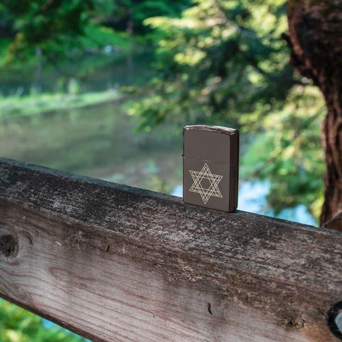 Lifestyle image of Star of David Design Black Ice® Windproof Lighter, standing on a railing outside with water and trees in the background.